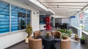 A modern indoor seating area with glass-top tables and cushioned chairs, a Coca-Cola vending machine, and potted plants.