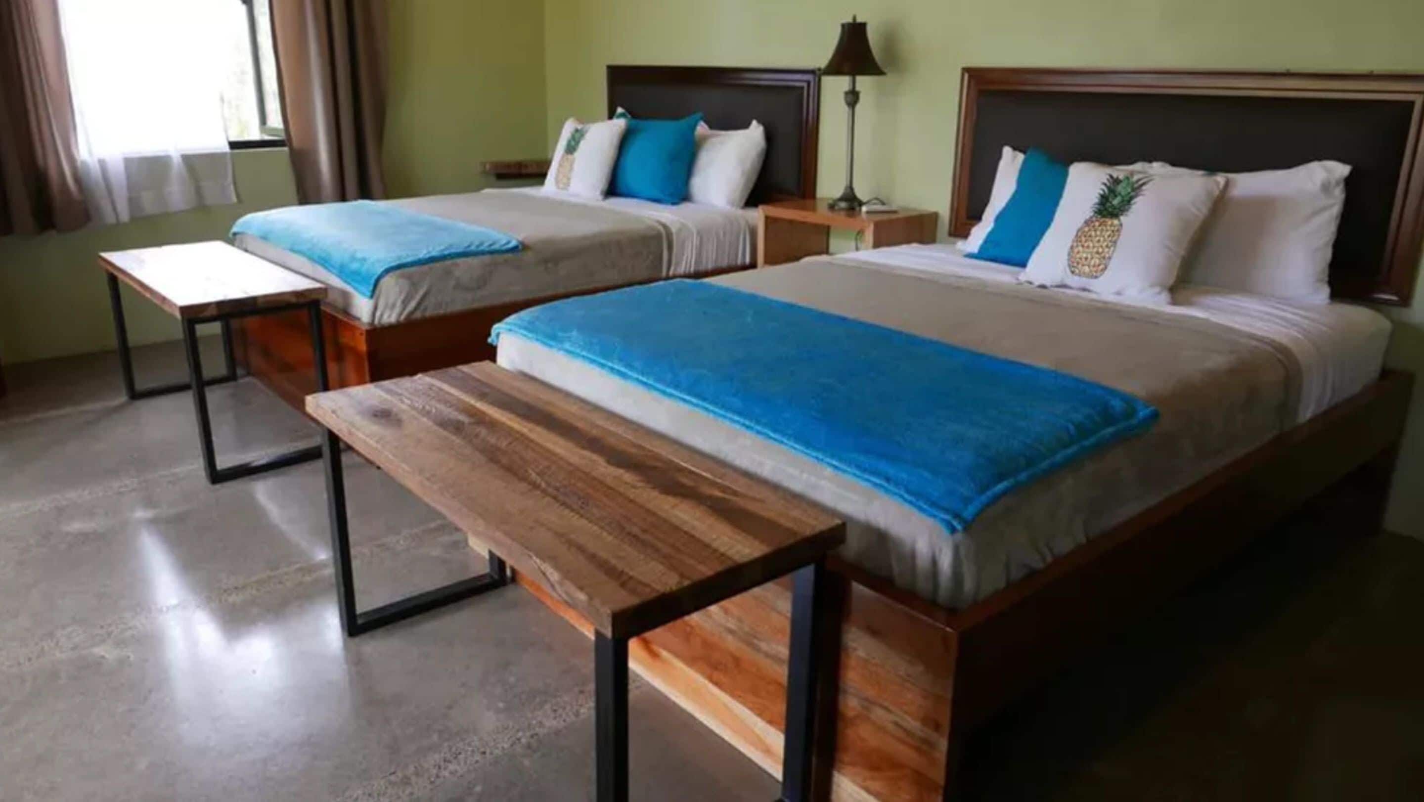 A hotel room with two beds, each with a wooden headboard, a bench, and a nightstand.