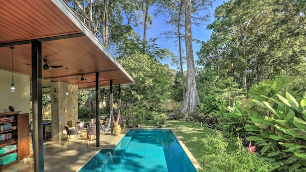 A swimming pool with a wooden deck and lounge area, surrounded by lush greenery and tall trees. - Villas Piña - Adults Only (Cahuita)