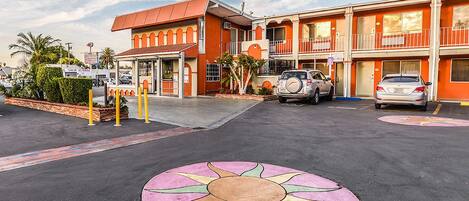 A motel with a red facade, a parking lot with a sun design, and two-story buildings.