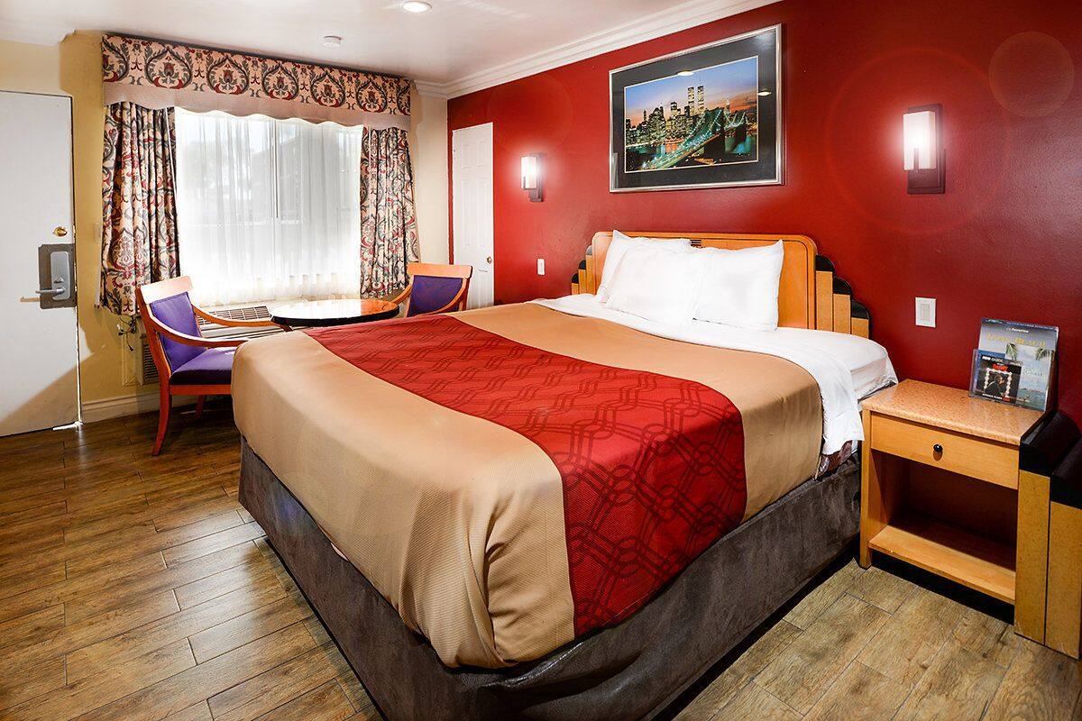 A hotel room with a large bed, a desk with a chair, a window with curtains, and a painting on the wall.