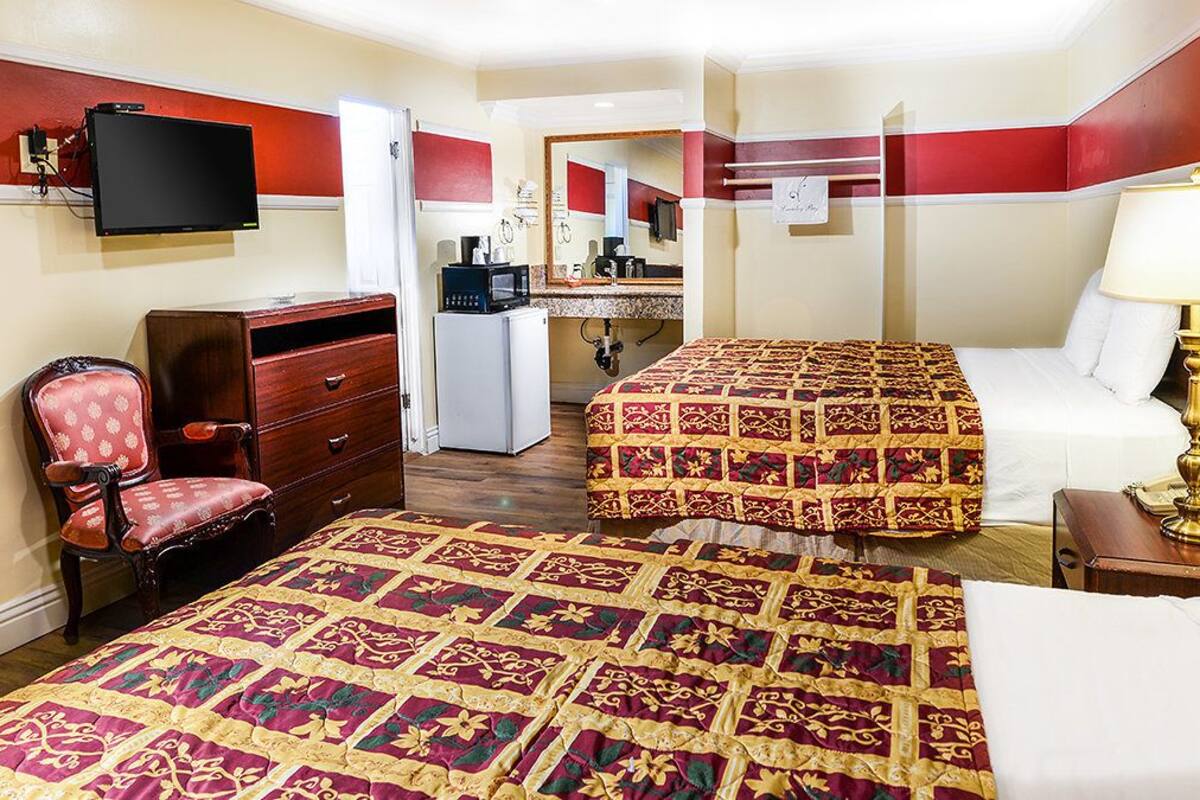 A hotel room with two beds, a desk with a computer, a chair, and a TV.