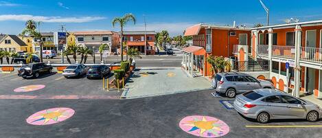 A parking lot with cars, a building with a red facade, and palm trees.