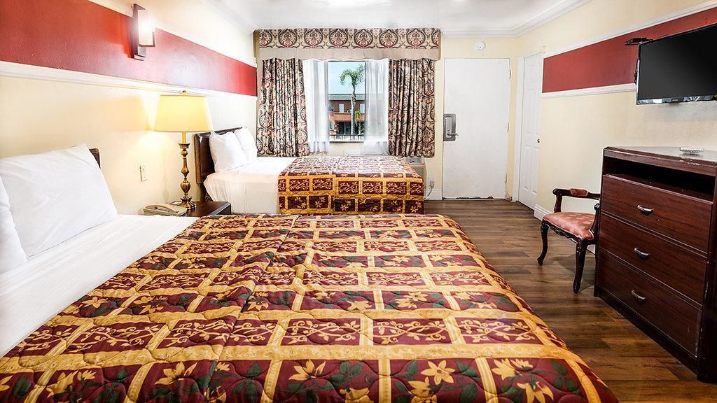 Une chambre d’hôtel avec deux lits, un bureau, une chaise, une télévision et une fenêtre avec des rideaux.