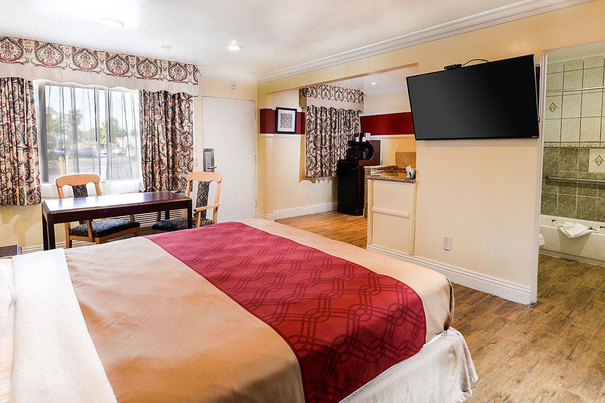 A hotel room with a large bed, a desk, a television, and a kitchenette.
