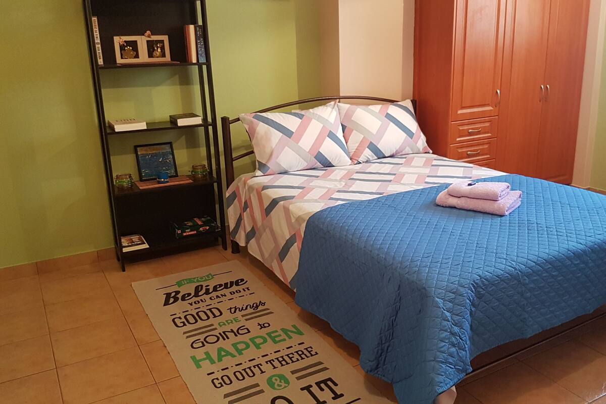 Ein Schlafzimmer mit Bett, Bücherregal, Kleiderschrank und einem Teppich mit Motiv.