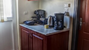 Et lille køkken med træskabe, kaffemaskine og elkedel på bordet.