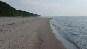 A wide sandy beach with gentle waves, a clear sky, and a forested hillside in the background. - Martha's Vineyard Bed & Breakfast (South Haven)