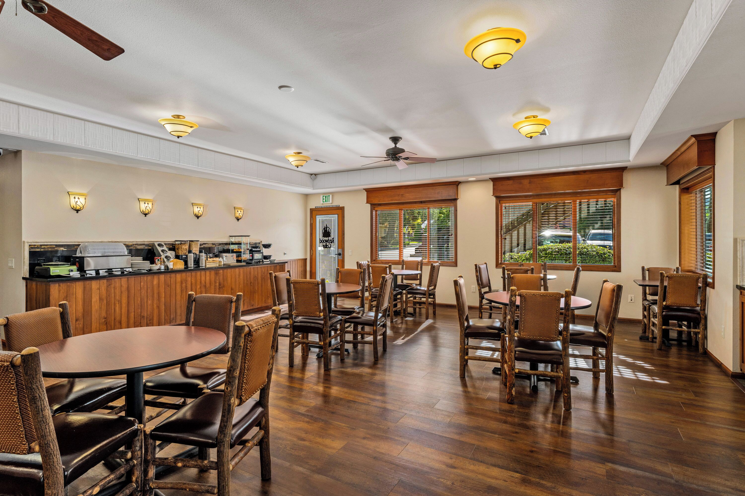 Un restaurante con mobiliario de madera, una zona de bar y ventanas grandes.