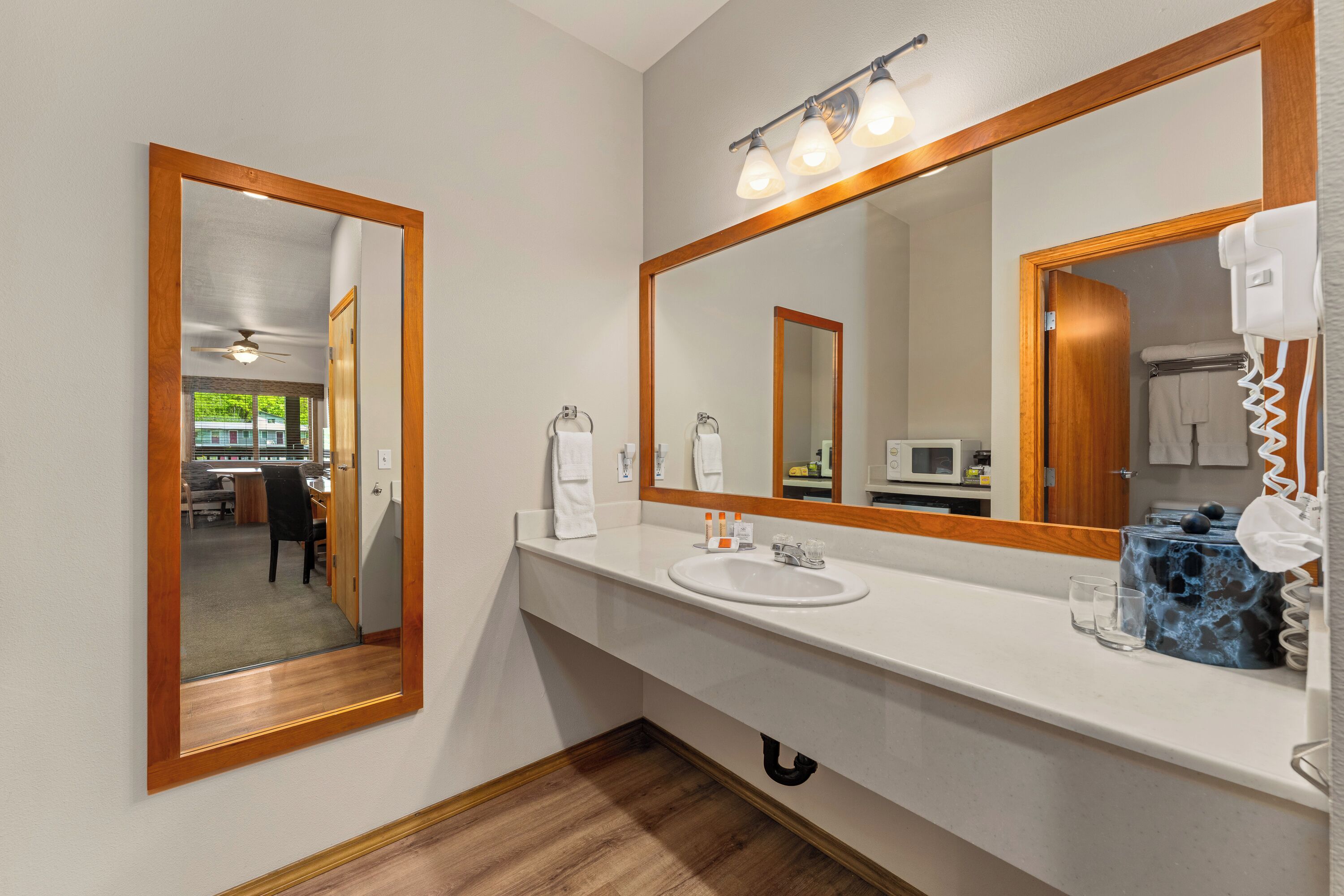 Een badkamer met een grote spiegel, een wit wastafeltje en een haardroger.