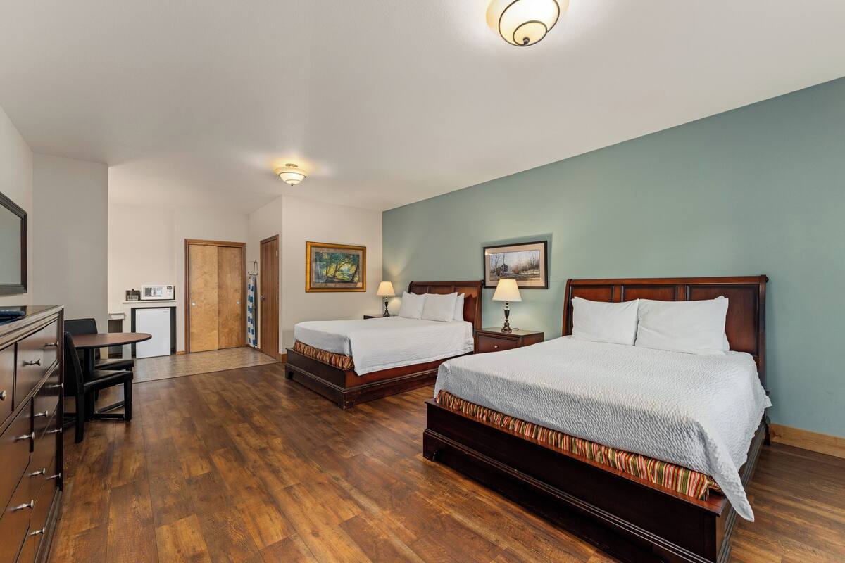A hotel room with two beds, a desk, a chair, a microwave, and a door leading to a bathroom.