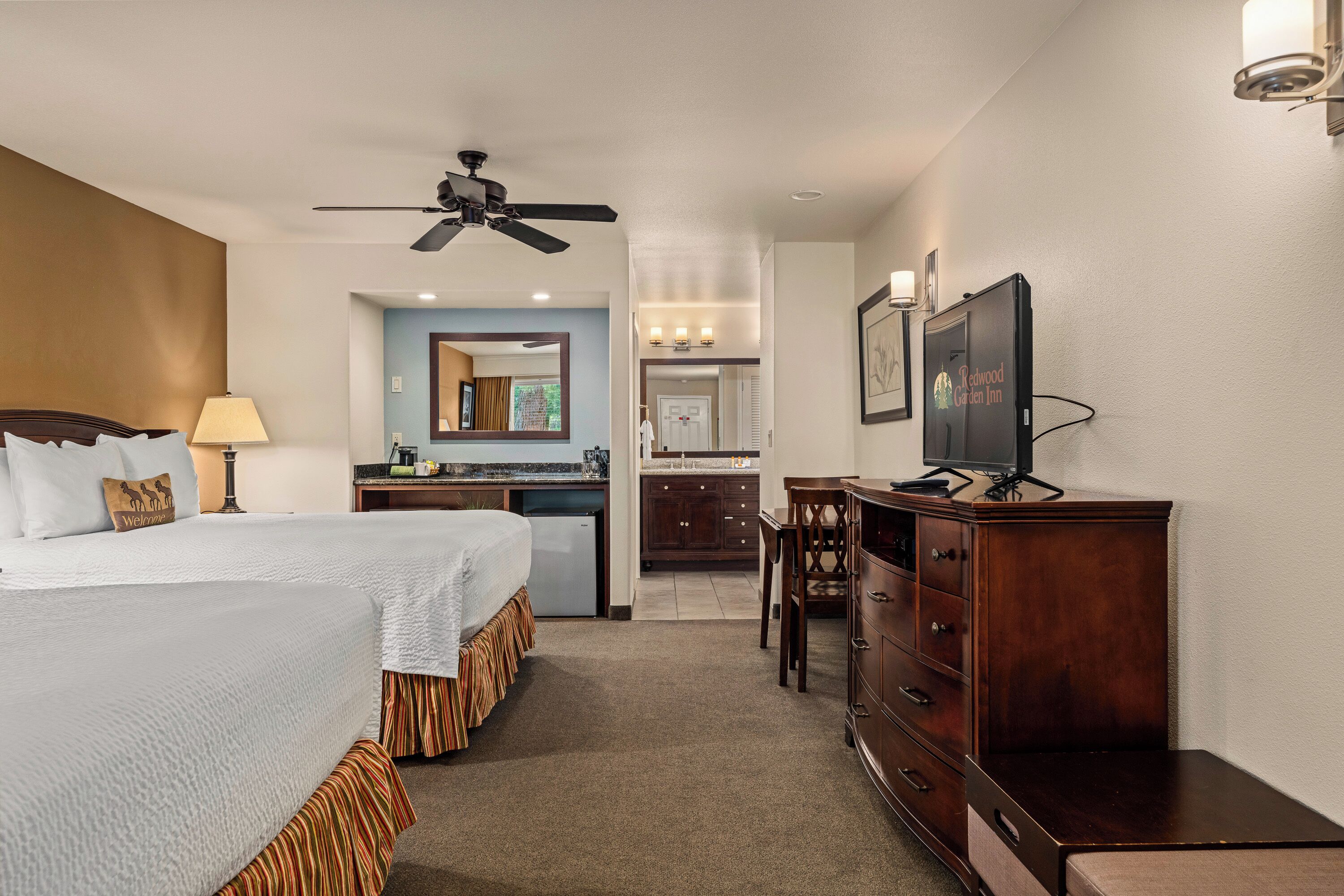 Une chambre d’hôtel avec un lit, un bureau, une télévision, un ventilateur de plafond et une salle de bain visible au fond.