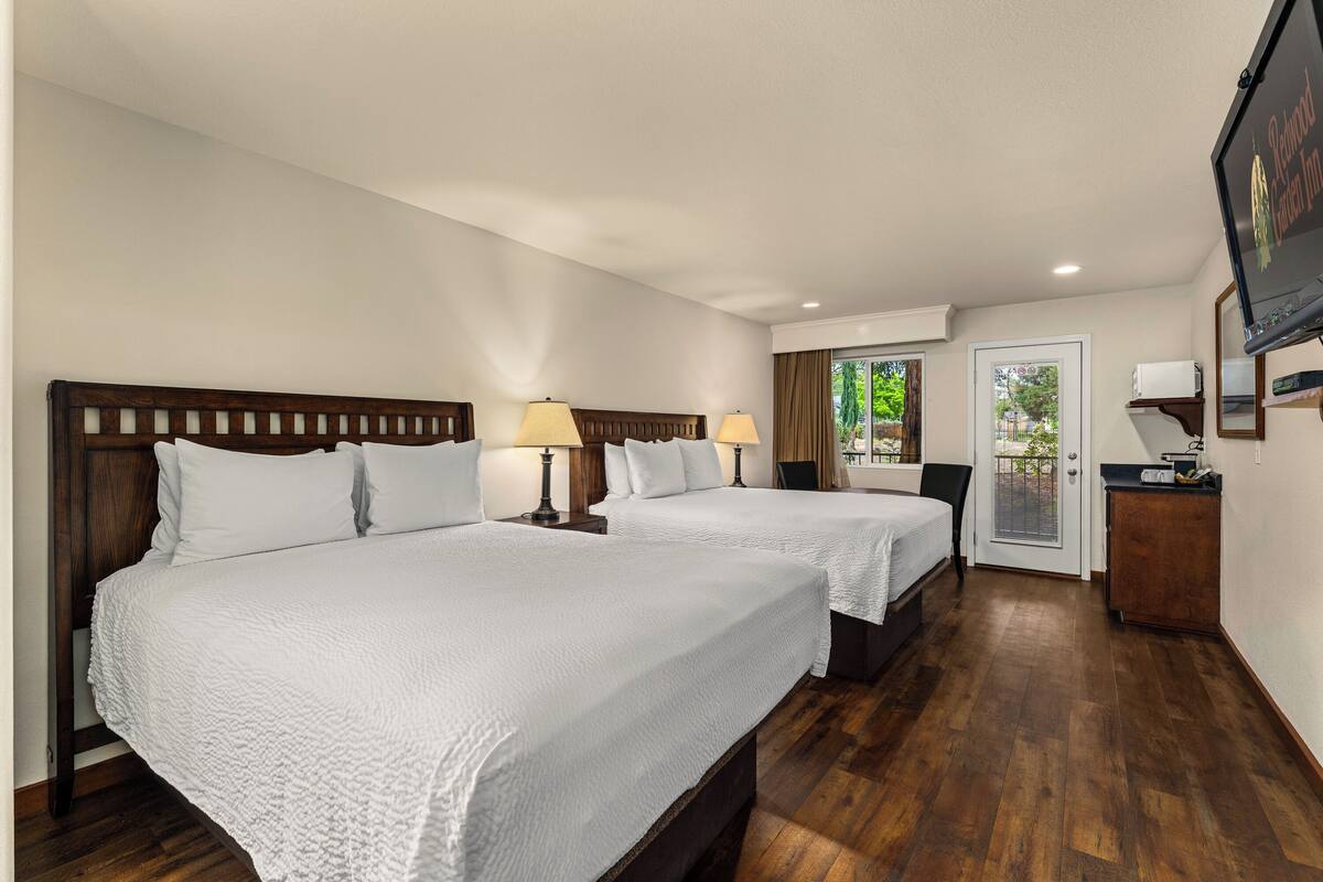 A hotel room with two beds, a TV, a desk, and a door leading to a balcony.