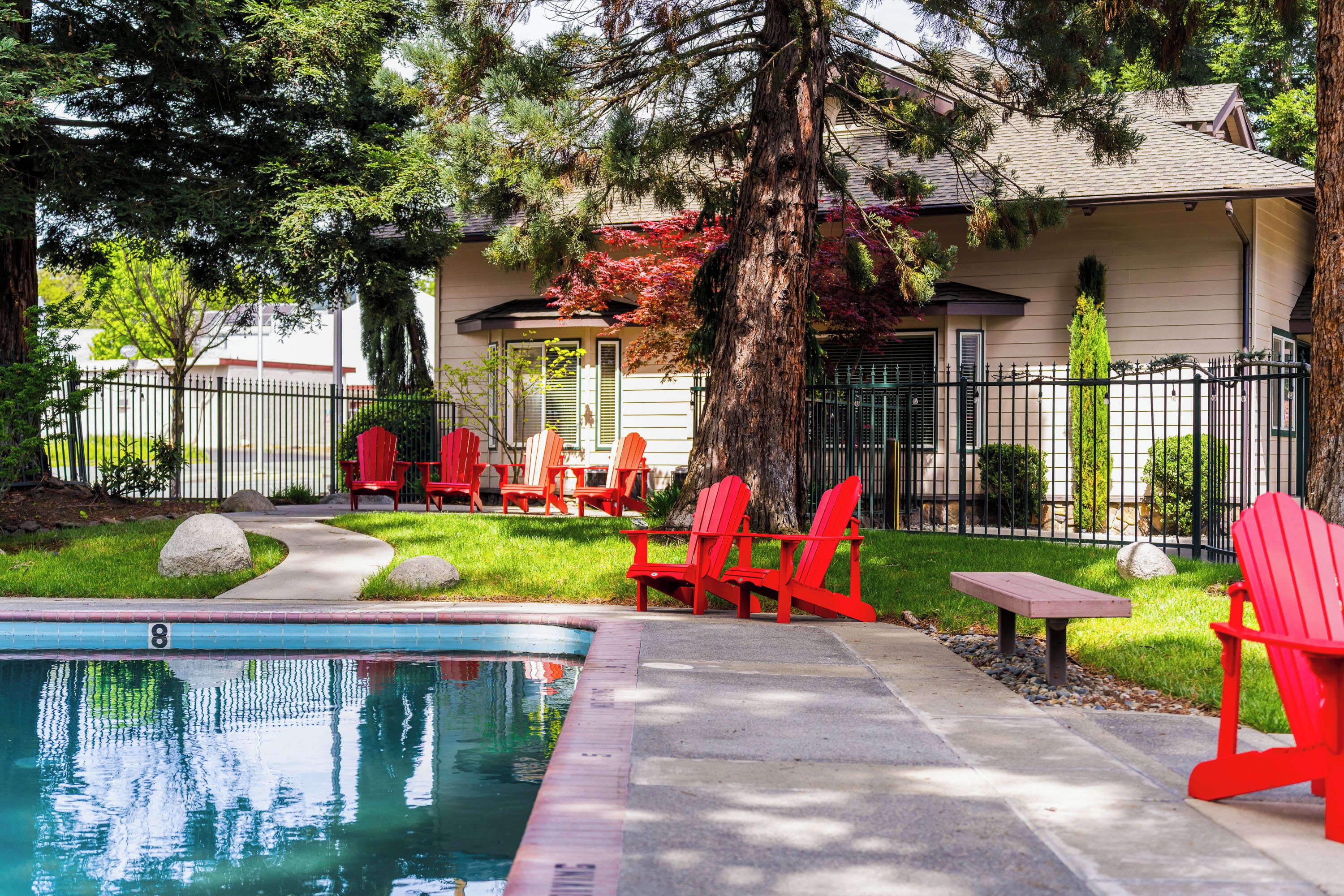 Ein Swimmingpool mit roten Adirondack-Stühlen, einer Steinsitzbank und einem Haus mit Baum im Hintergrund.