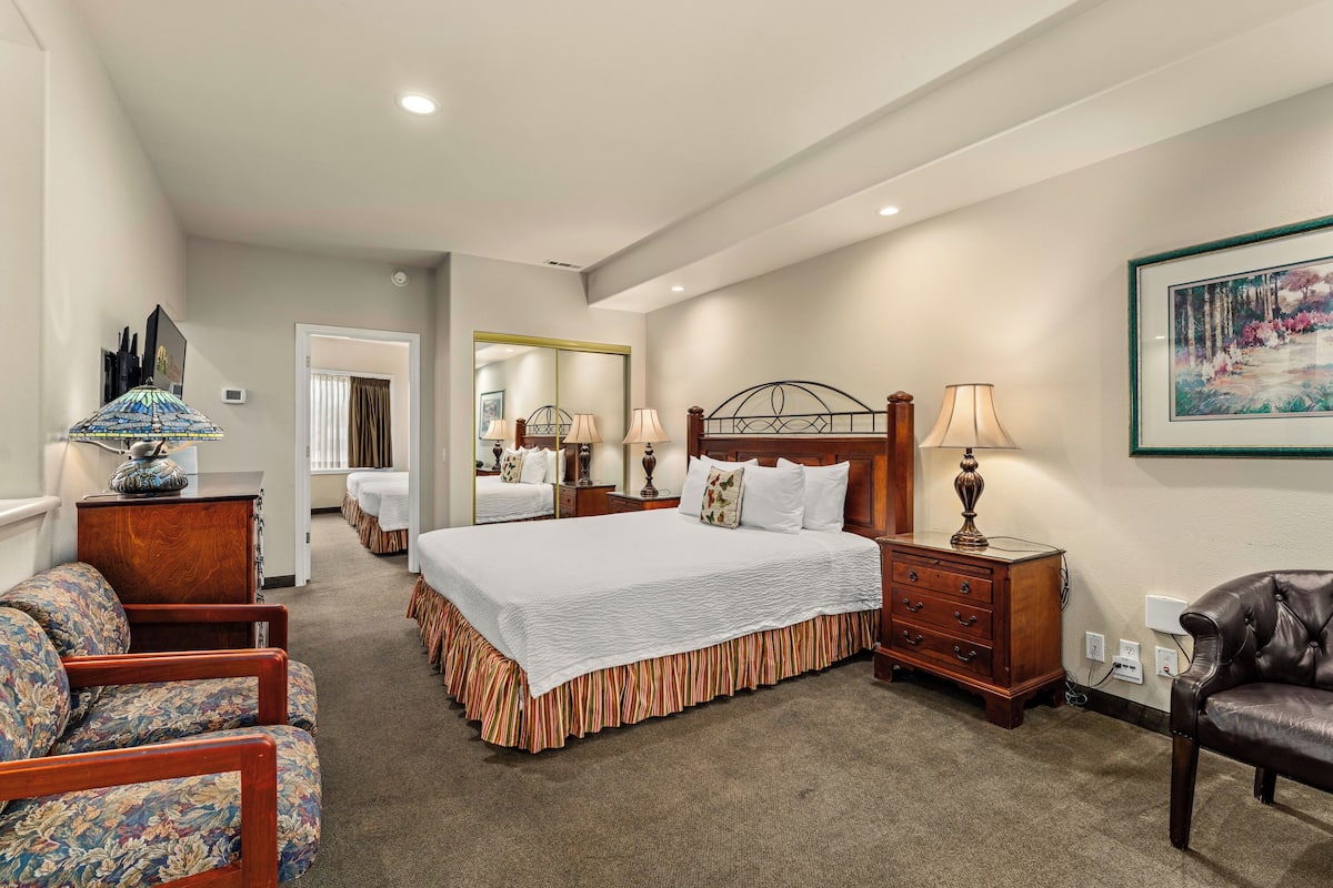 A hotel room with a large bed, a wooden nightstand, a chair, a desk, a mirror, and a painting on the wall.