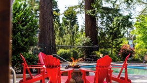 A poolside area with red Adirondack chairs, a fire pit, and a pool. - Redwood Garden Inn (Grants Pass)