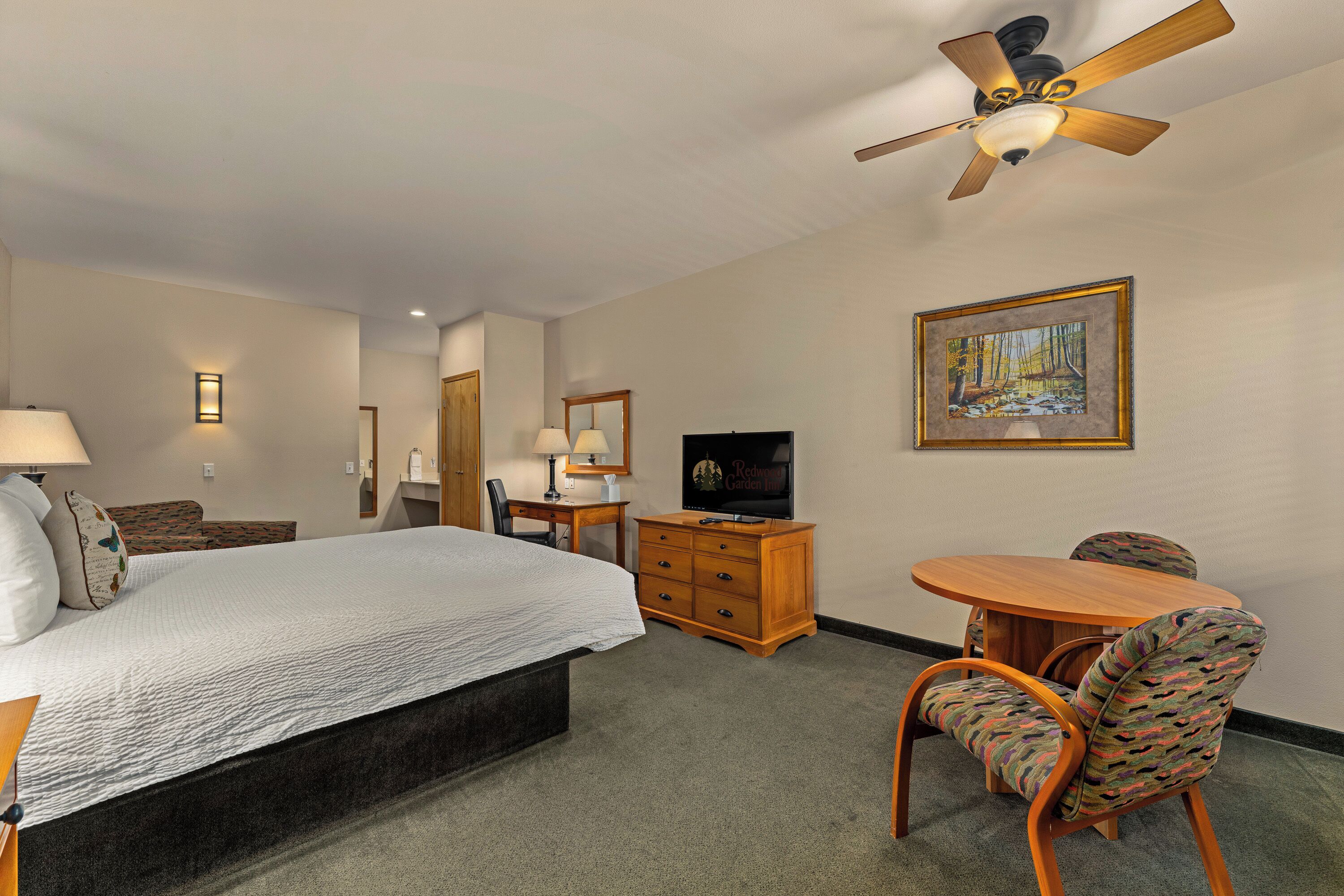 Habitación de hotel con cama, escritorio, silla, televisor y ventilador de techo.