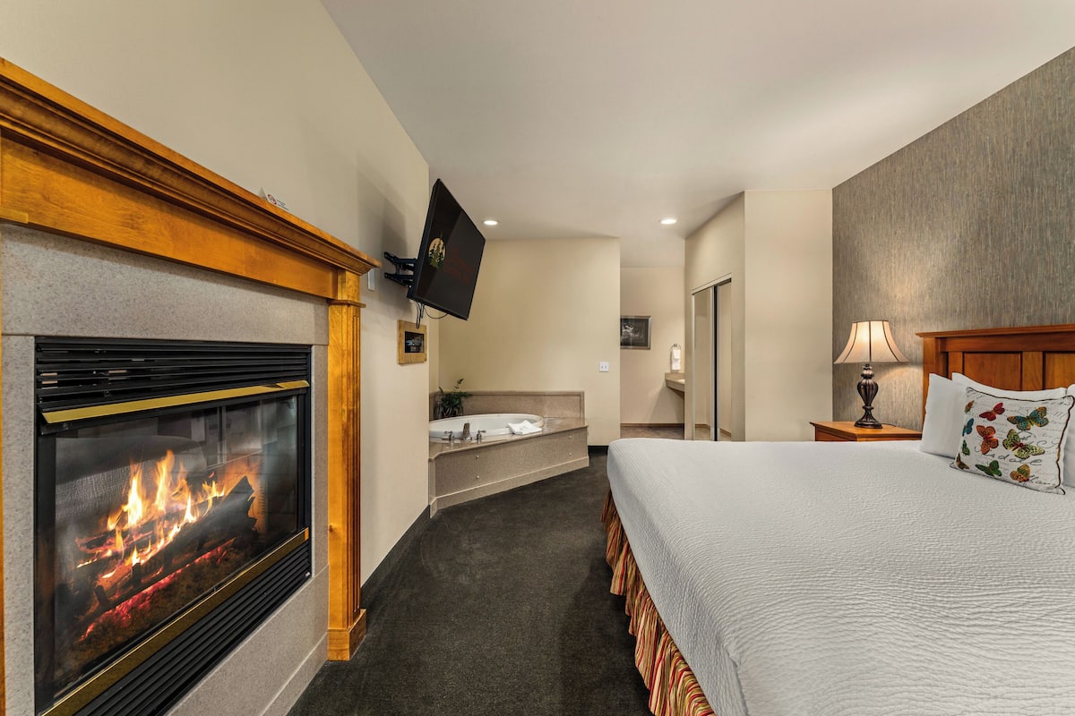 A hotel room with a fireplace, a bed, a television, a bathroom, and a nightstand.