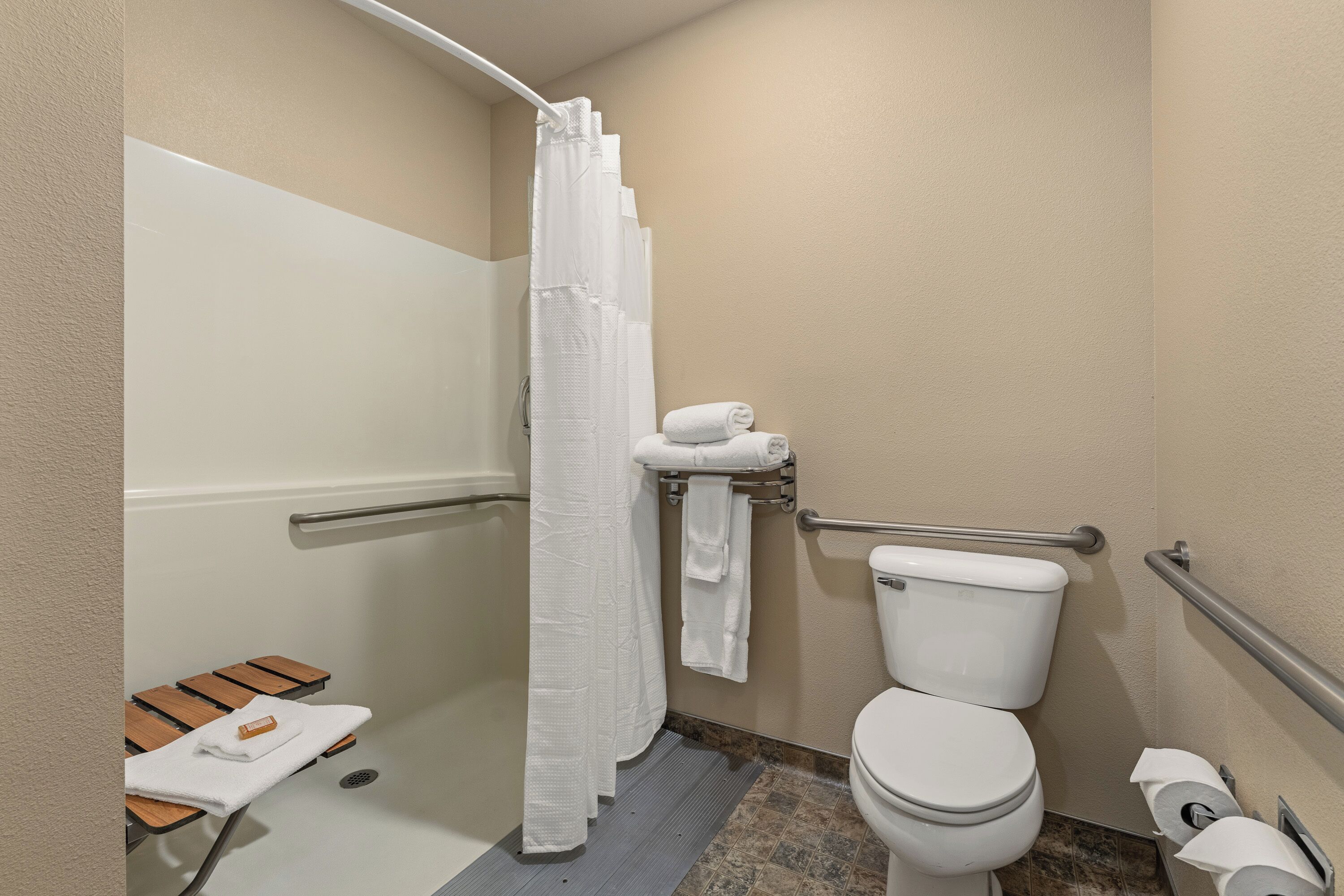 Un baño con ducha, inodoro y barras de apoyo.
