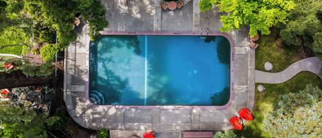 An aerial view of a swimming pool with surrounding patio furniture and greenery.