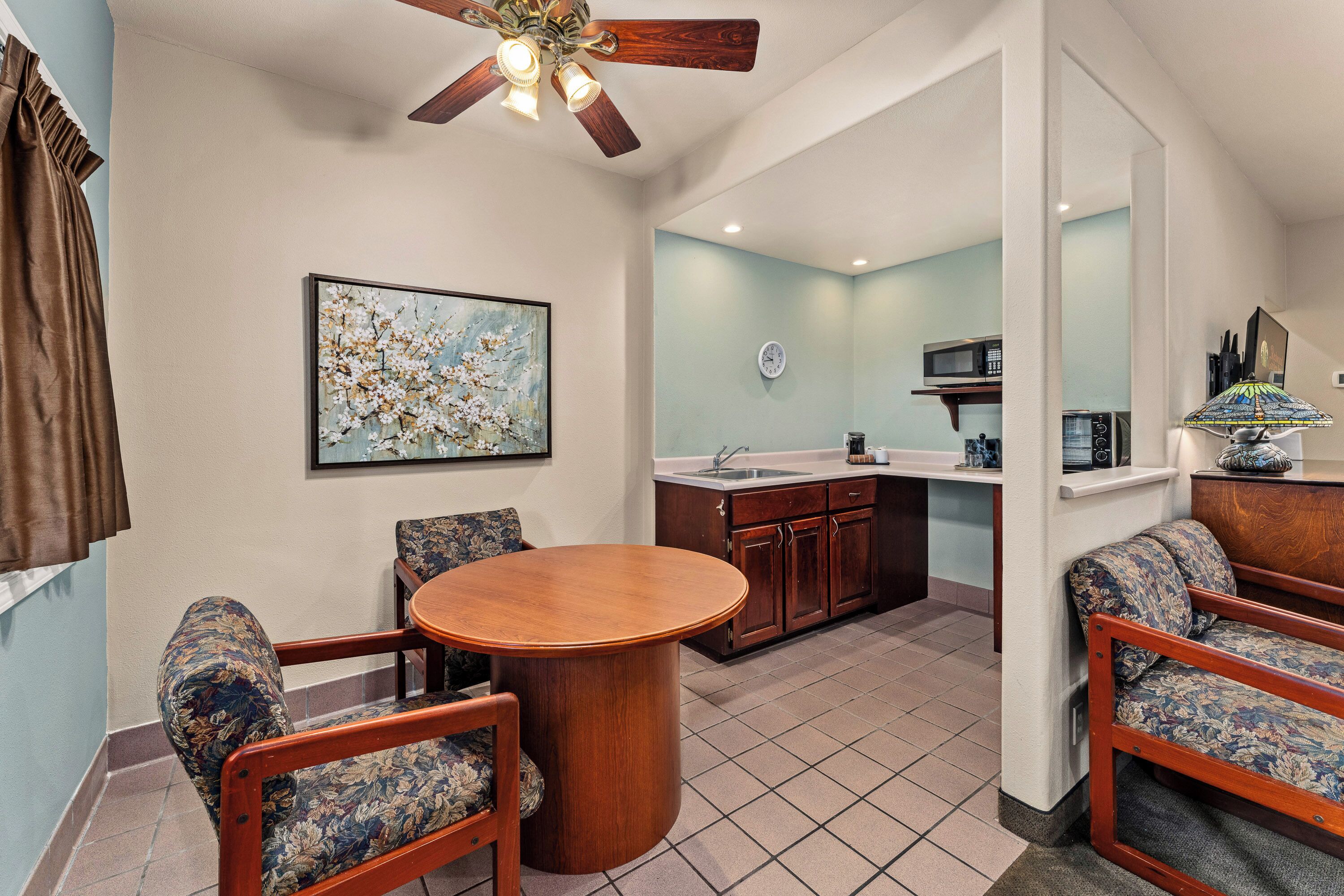A dining area with a round table and chairs, a ceiling fan, a kitchen with a microwave and sink, and a sofa.