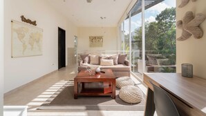 A modern living room with a large window, a world map, a ceiling fan, and a sofa with cushions. - Meso Maya (Tulum)