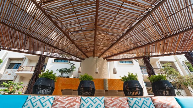 A covered outdoor seating area with a bamboo roof, potted plants, and patterned cushions. - Amazing Tulum swim explore cycle by BRM (Tulum)