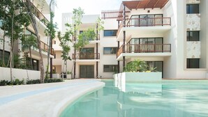 A modern building with multiple balconies, a swimming pool, and lush greenery. - Amazing Tulum swim explore cycle by BRM (Tulum)