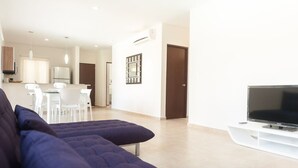 A modern living room with a large flat-screen TV, a sofa, and a dining area with chairs and a table. - Amazing Tulum swim explore cycle by BRM (Tulum)