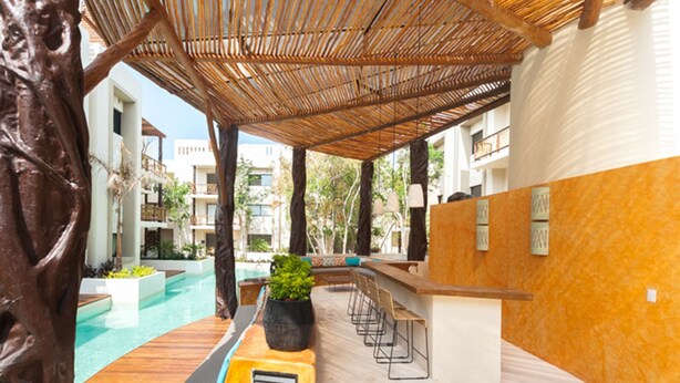 A poolside area with a wooden deck, a bar with stools, and a seating area with a plant. - Prana 212 by BRM (Tulum)