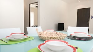 A dining table set with white bowls and red-rimmed plates, green placemats, and a woven basket. - Prana 212 by BRM (Tulum)
