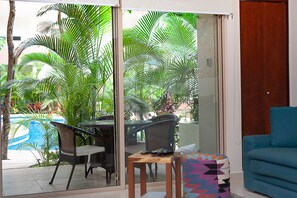 A room with a glass door leading to a pool area, a blue sofa, and a small table with chairs. - Puerta Zama 107 by BRM (Tulum)