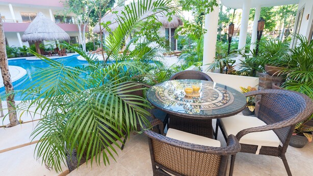 Un espace extérieur aménagé dans un style tropical, avec une table ronde, des chaises en osier et une piscine en arrière-plan.