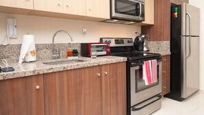 Une cuisine moderne avec des meubles en bois, un four à micro-ondes en acier inoxydable, un grille-pain rouge, une bouilloire et un réfrigérateur noir.