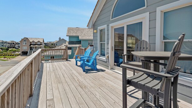 A wooden deck with outdoor furniture, a covered area, and a view of neighboring buildings. - Dolphin Waves: Oceanside, Private Pool & Spa, Close to Beach, Quiet Neighborhood (Nags Head)