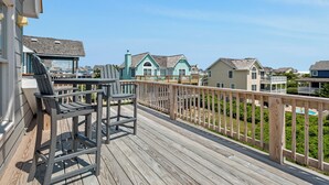 A wooden deck with chairs, a pool, and houses in the background. - Dolphin Waves: Oceanside, Private Pool & Spa, Close to Beach, Quiet Neighborhood (Nags Head)