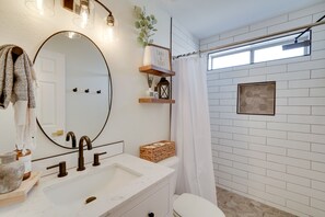 Et moderne badeværelse med en hvid kommode, et stort spejl og en bruser med hvidt gardin.