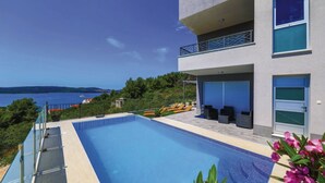 A modern building with a swimming pool, a balcony with outdoor seating, and a view of the sea. - Holiday Home Goldy Trogir-Čiovo (Trogir)