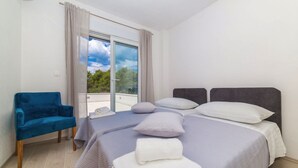 A bedroom with two beds, a blue chair, and a large window with curtains. - Holiday Home Goldy Trogir-Čiovo (Trogir)