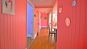 A hallway with pink walls, wooden flooring, and a dining area with a table and chairs. - Historic Apartment in the Center of Christiansted (Christiansted)