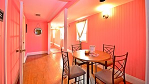 A room with pink walls, a wooden floor, a round table with chairs, and a mirror on the wall. - Historic Apartment in the Center of Christiansted (Christiansted)