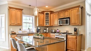 A spacious kitchen with wooden cabinets, a granite countertop, and a central island with bar stools. - Colonial-Style 'Warwick Retreat' - 1 Hour to NYC! (Monroe)