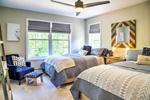 Ein Schlafzimmer mit zwei Betten, einem Sessel, einer Bank, einem Deckenventilator und einem Fenster mit Blick ins Grüne.