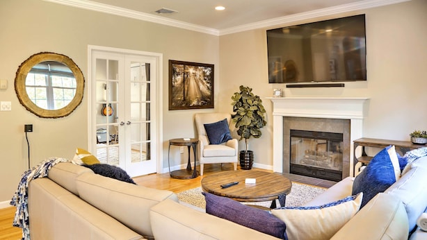 A living room with a beige sofa, a round coffee table, a fireplace, and a large TV mounted above the fireplace. - Colonial-Style 'Warwick Retreat' - 1 Hour to NYC! (Monroe)