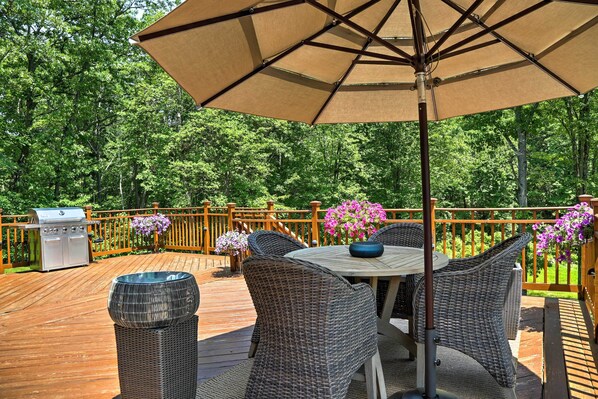 Eine Holzterrasse mit Korbmöbeln, einem Grill und Topfpflanzen.