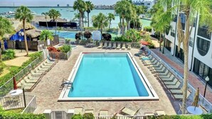 Ein rechteckiger Pool mit einer umlaufenden Liegefläche, Liegestühlen und Palmen.