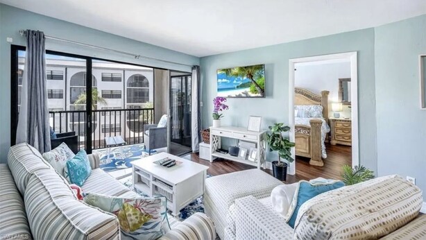 Ein geräumiges Wohnzimmer mit Balkon, einem Essbereich und einem durchgehenden offenen Tür sichtbaren Schlafzimmer.