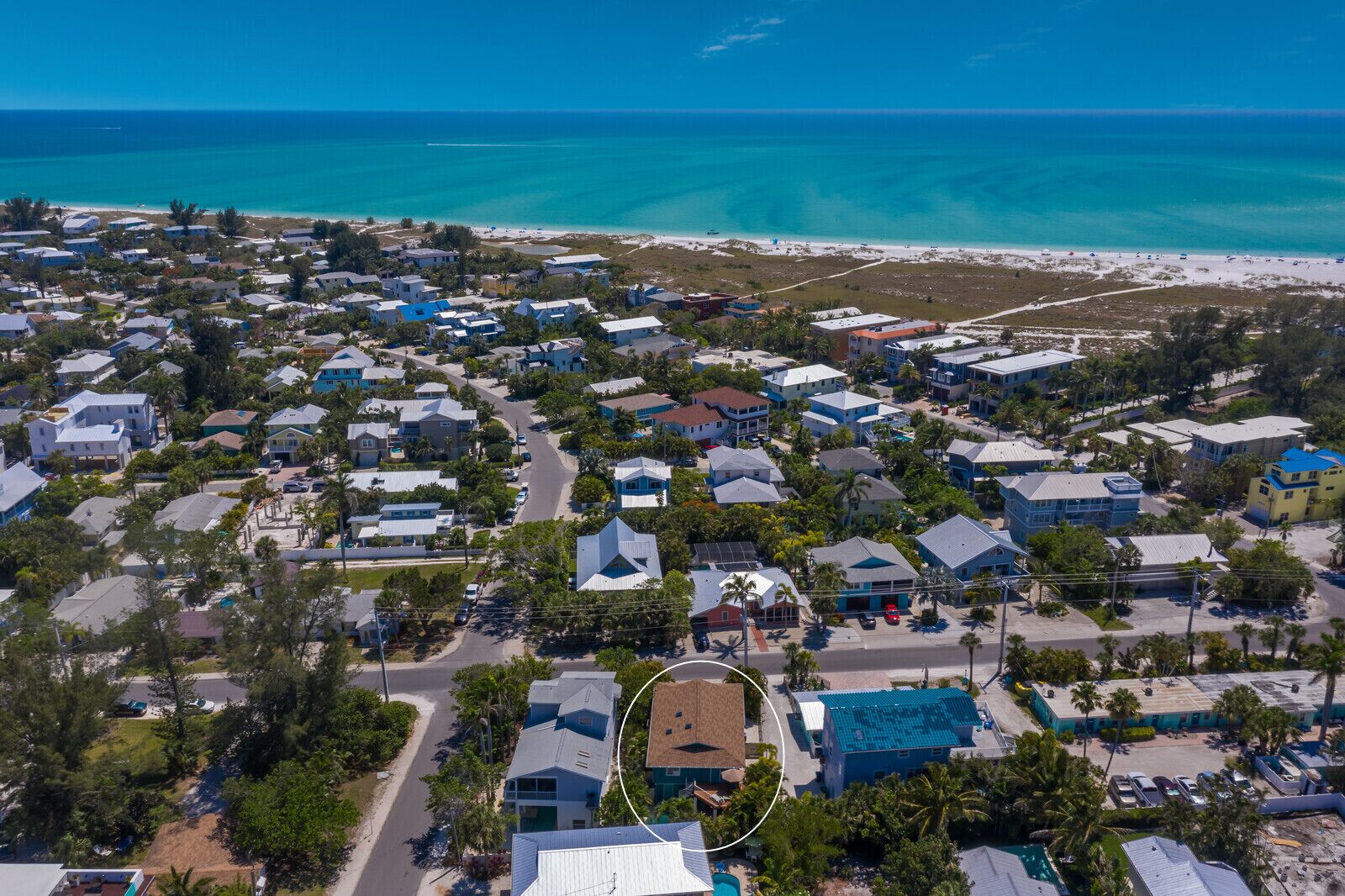 An aerial view of a coastal residential area with houses, roads, and a beach.