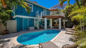 Une piscine avec une terrasse en bois, un escalier en colimaçon blanc et du mobilier d’extérieur.