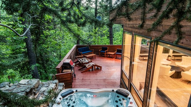 Een houten terras met buitenmeubilair, een jacuzzi en een glazen ruimte met moderne inrichting.